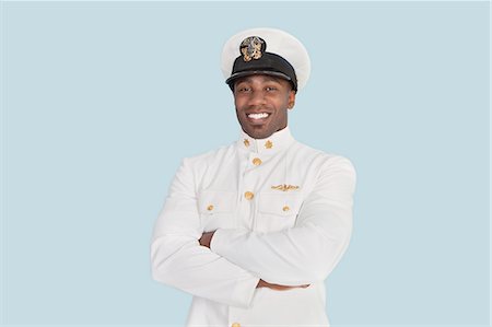 Portrait d'un jeune officier de marine américaine heureux avec les bras croisés sur fond bleu clair Photographie de stock - Premium Libres de Droits, Code: 693-06379105