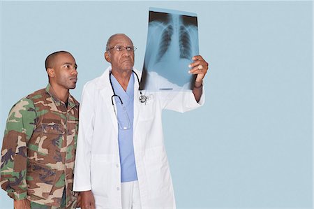 Senior doctor with soldier looking at x-ray report, Studio Shot on light blue background Foto de stock - Sin royalties Premium, Código: 693-06379132