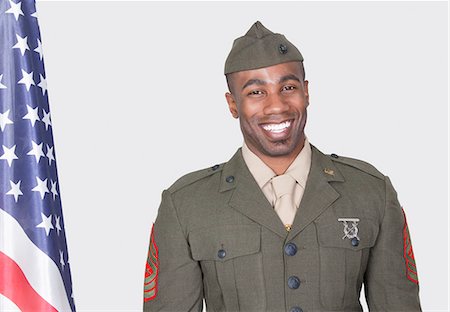 Porträt eines männlichen US-Soldaten lächelnd mit der amerikanischen Flagge auf grauem Hintergrund Stockbilder - Premium RF Lizenzfrei, Bildnummer: 693-06379159