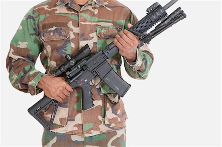 soldier standing with gun - Midsection of soldier holding M4 assault rifle, Studio Shot on gray background Stock Photo - Premium Royalty-Free, Code: 693-06379152