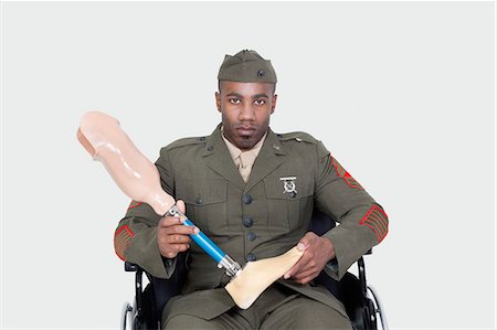 Portrait of military officer in wheelchair holding prosthesis foot, Studio Shot on gray background Foto de stock - Sin royalties Premium, Código: 693-06379164