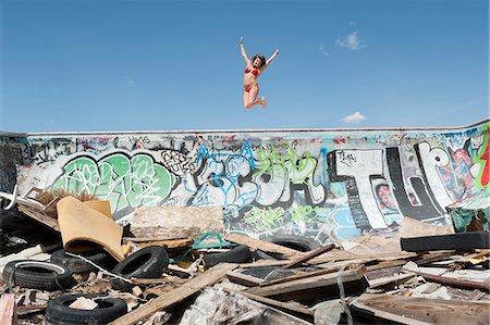 simsearch:693-06379200,k - Young woman in bikini jumping over graffiti wall with garbage in foreground Stock Photo - Premium Royalty-Free, Code: 693-06379188