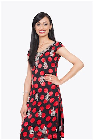 simsearch:693-06379274,k - Portrait of Indian woman smiling with hand on hip against gray background Fotografie stock - Premium Royalty-Free, Codice: 693-06379293