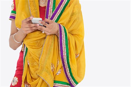 Midsection of woman in Indian clothing using cell phone over white background Stock Photo - Premium Royalty-Free, Code: 693-06379328