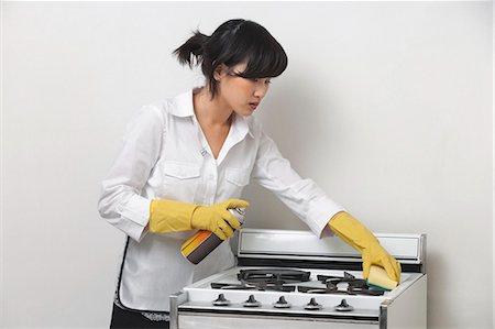 Young housemaid cleaning stove against gray background Stock Photo - Premium Royalty-Free, Code: 693-06379374