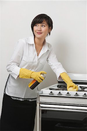 Young maidservant looking away while cleaning stove against gray background Foto de stock - Sin royalties Premium, Código: 693-06379377