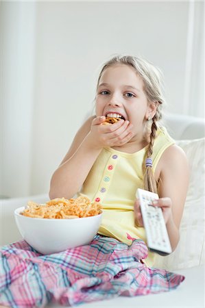 eating sofa - Girl watching TV as she stuffs her mouth with wheel shape snack pellets Stock Photo - Premium Royalty-Free, Code: 693-06379390