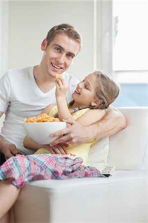 smiling kid eating bowl - Daughter feeding wheel shape snack pellets to her father Stock Photo - Premium Royalty-Free, Code: 693-06379393