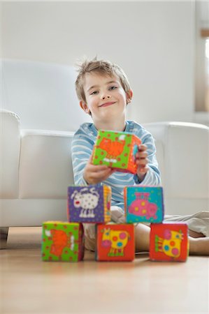 Portrait of cute little boy stacking blocks while sitting on floor Stock Photo - Premium Royalty-Free, Code: 693-06379405