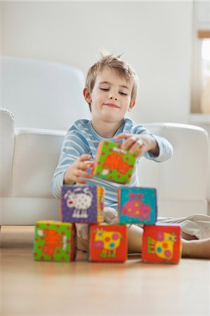 Little boy stacking blocks while sitting on floor Stock Photo - Premium Royalty-Free, Code: 693-06379407