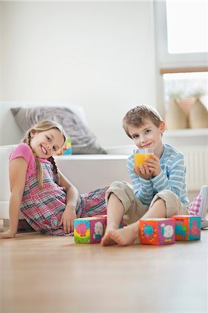 Portrait of young boy drinking orange juice while sitting with sister on floor Stock Photo - Premium Royalty-Free, Code: 693-06379403