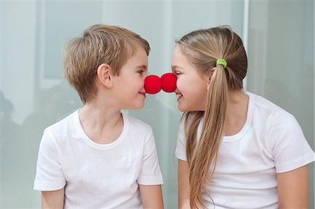 picture of boy and girl smiling - Happy young siblings in white tshirts rubbing clown noses against each other Stock Photo - Premium Royalty-Free, Code: 693-06379434