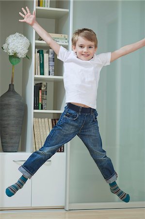 Portrait d'un garçon en employés occasionnels sautant dans les airs à la maison Photographie de stock - Premium Libres de Droits, Code: 693-06379446