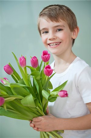 Portrait of happy young boy holding bunch of pink tulips against gray background Stock Photo - Premium Royalty-Free, Code: 693-06379442