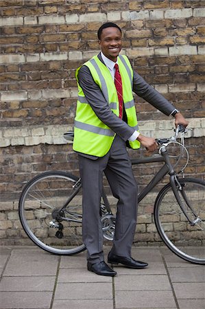 simsearch:693-06379459,k - Happy young male engineer with bicycle against brick wall Stock Photo - Premium Royalty-Free, Code: 693-06379475