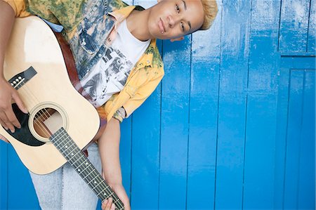 simsearch:695-05764970,k - Portrait of a teenage boy playing guitar against wood paneled wall Stock Photo - Premium Royalty-Free, Code: 693-06379489