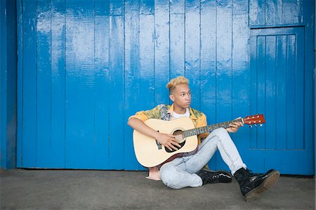 simsearch:693-06379581,k - Trendy teenage boy playing guitar as he sits against wood paneled wall Foto de stock - Sin royalties Premium, Código: 693-06379490