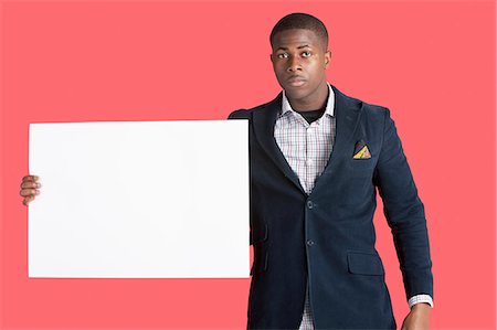 Portrait of a young smart man wearing coat with blank cardboard over pink background Stock Photo - Premium Royalty-Free, Code: 693-06379534