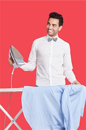 planchar - Happy man in formals ironing shirt over red background Foto de stock - Sin royalties Premium, Código: 693-06379539