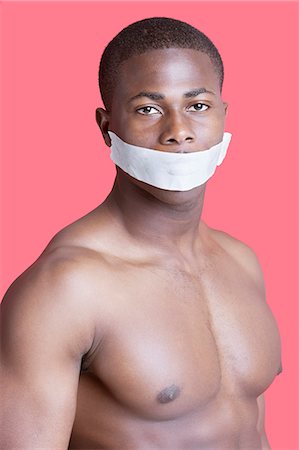 forbidding - Portrait of shirtless African American man with tape over mouth against pink background Stock Photo - Premium Royalty-Free, Code: 693-06379531
