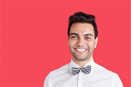 Portrait of a happy mid adult man wearing bow-tie over red background Stock Photo - Premium Royalty-Free, Code: 693-06379545