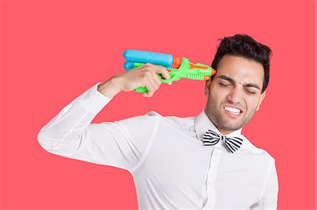 revolver - Homme frustré tenant arme-jouet à sa tête sur fond rouge Photographie de stock - Premium Libres de Droits, Code: 693-06379541