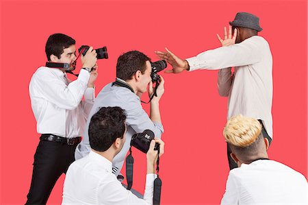 paparazzi - Young male celebrity shielding face from photographers over red background Foto de stock - Sin royalties Premium, Código: 693-06379566