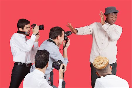 sesión fotográfica - Young male celebrity shielding face from photographers over red background Foto de stock - Sin royalties Premium, Código: 693-06379567