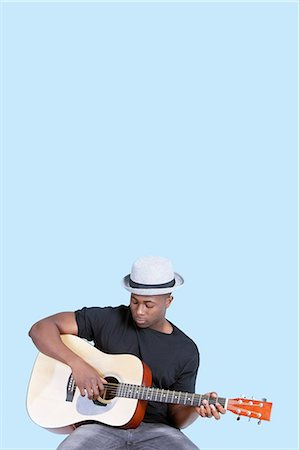playing music - Young African American man playing guitar over light blue background Stock Photo - Premium Royalty-Free, Code: 693-06379571