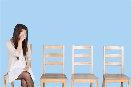 photographs of sad waiting women - Young woman crying besides empty wooden chairs over blue background Stock Photo - Premium Royalty-Free, Code: 693-06379591