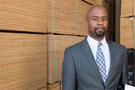 Portrait of an African American businessman standing in front of stacked wooden planks Stock Photo - Premium Royalty-Free, Code: 693-06379693