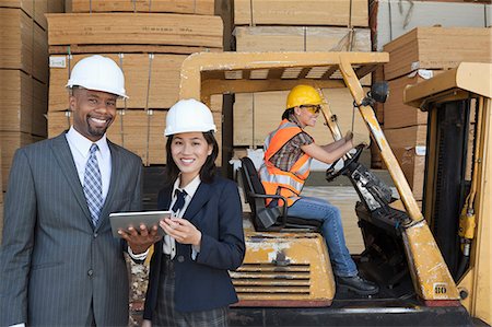 simsearch:693-06379749,k - Happy multiethnic engineers holding tablet PC with female worker driving forklift truck in background Stock Photo - Premium Royalty-Free, Code: 693-06379709