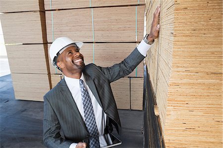 Happy African American male contractor inspecting wooden planks while holding tablet PC Stock Photo - Premium Royalty-Free, Code: 693-06379714