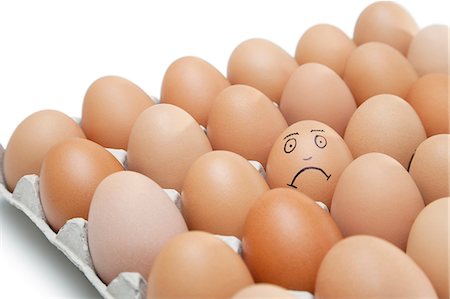 egg tray - Triste visage dessiné sur un oeuf entouré de œufs bruns clair en carton sur fond blanc Photographie de stock - Premium Libres de Droits, Code: 693-06379766