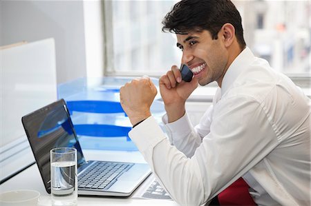 simsearch:693-06379784,k - Excited businessman using cell phone at office desk Fotografie stock - Premium Royalty-Free, Codice: 693-06379784