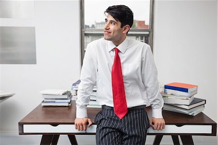 Indischer Geschäftsmann stützte sich auf Schreibtisch, während im Büro Wegsehen Stockbilder - Premium RF Lizenzfrei, Bildnummer: 693-06379801