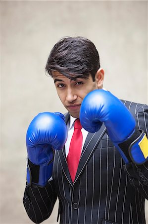 Portrait of an Indian businessman wearing blue boxing gloves against gray background Stock Photo - Premium Royalty-Free, Code: 693-06379819