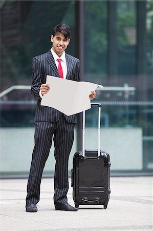 Young Indian businessman with luggage bag reading paper Stock Photo - Premium Royalty-Free, Code: 693-06379810