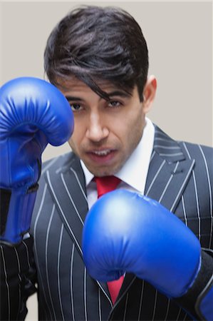 Portrait of an Indian businessman wearing blue boxing gloves against gray background Stock Photo - Premium Royalty-Free, Code: 693-06379821