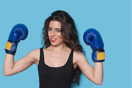 pugilista (mujer) - Portrait of a beautiful young female boxer raising arms in victory against blue background Foto de stock - Sin royalties Premium, Código: 693-06379855