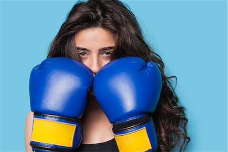 portrait of woman boxer - Portrait of a young female boxer with fists up against blue background Stock Photo - Premium Royalty-Free, Code: 693-06379856