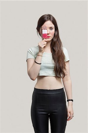 Portrait of beautiful young woman holding ice cream bar over eye against gray background Foto de stock - Sin royalties Premium, Código: 693-06379904