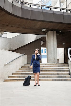 Young Indian businesswoman using cell phone with luggage outdoors Stock Photo - Premium Royalty-Free, Code: 693-06379900