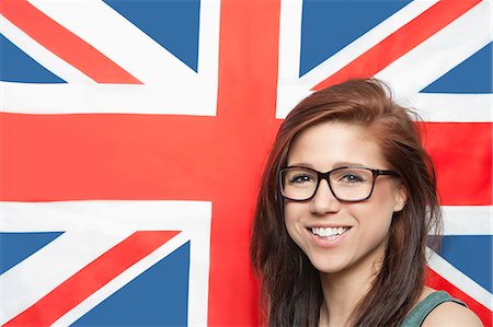 Portrait of cheerful young woman wearing eyeglasses against British flag Stock Photo - Premium Royalty-Free, Code: 693-06379919