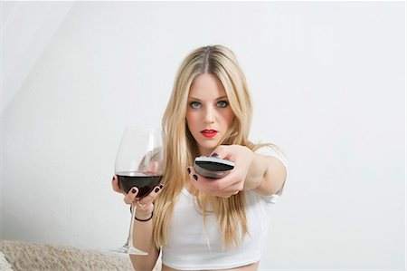 Portrait of a young woman holding wine glass while using remote control Stock Photo - Premium Royalty-Free, Code: 693-06379911