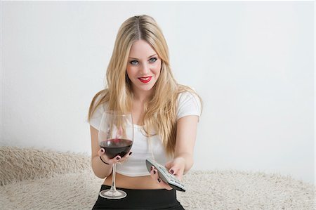 Happy young woman holding wine glass while watching television Stock Photo - Premium Royalty-Free, Code: 693-06379912