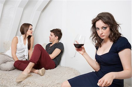 envie (jalousie) - Portrait d'une jeune femme irritée tenant un verre de vin avec couple en arrière-plan Photographie de stock - Premium Libres de Droits, Code: 693-06379960