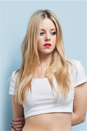 Beautiful blond woman with red lips looking down against light blue background Stock Photo - Premium Royalty-Free, Code: 693-06379992