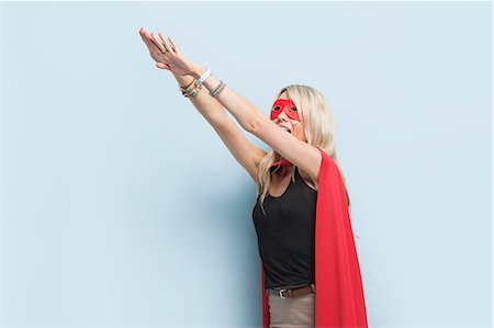 simsearch:693-06379982,k - Young woman in superhero outfit pretending to leap in the air against light blue background Stock Photo - Premium Royalty-Free, Code: 693-06379993