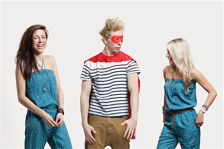 Young man in superhero costume standing with happy female friends in matching jump suits against gray background Foto de stock - Sin royalties Premium, Código: 693-06380018